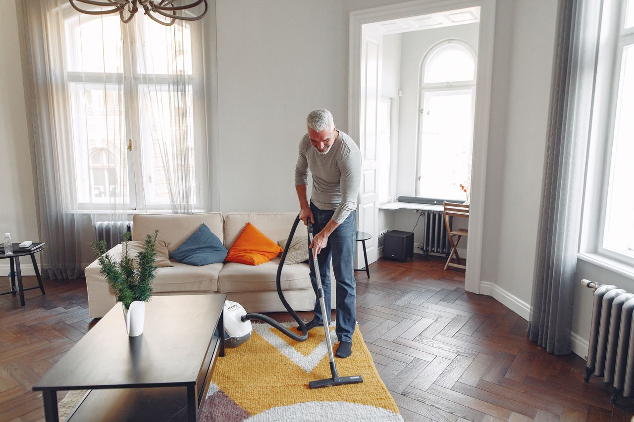 Vue en plongée d’un homme aux cheveux gris et à la barbe, aspirant le tapis chez lui