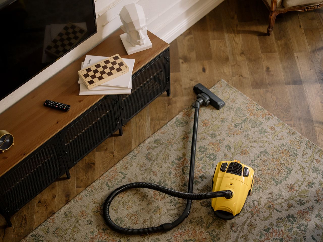 A cozy living room with a vintage feel, showing a yellow vacuum on a floral carpet.